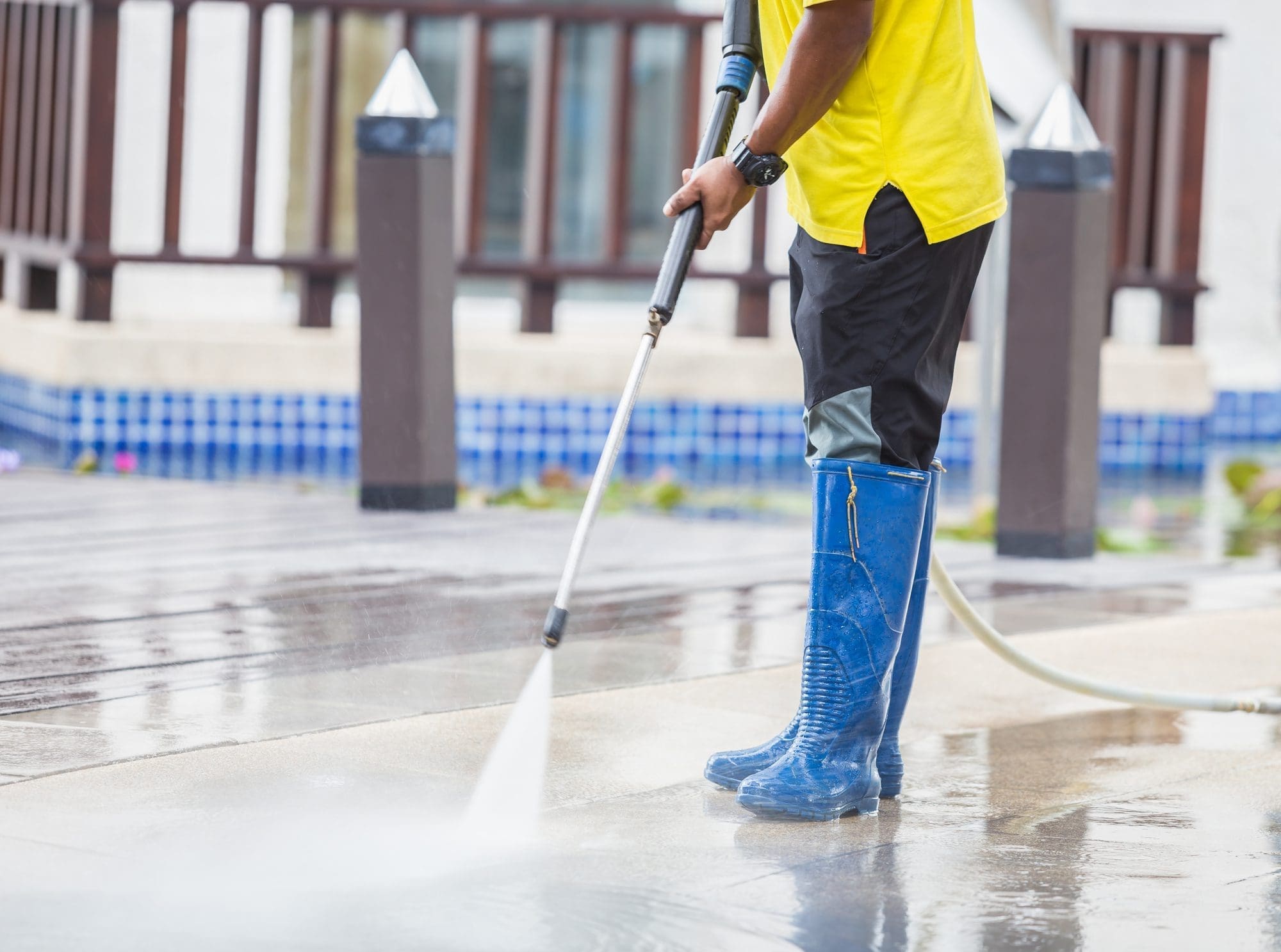 Man In Blue Boots And Yellow Shirt Power Washes An Outdoor Deck In Fellsmere